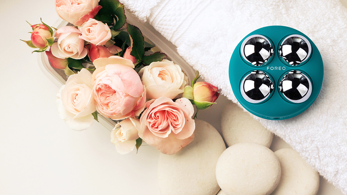 BEAR™ 2 body device on a fluffy white towel next to a bouquet of gorgeous pink roses